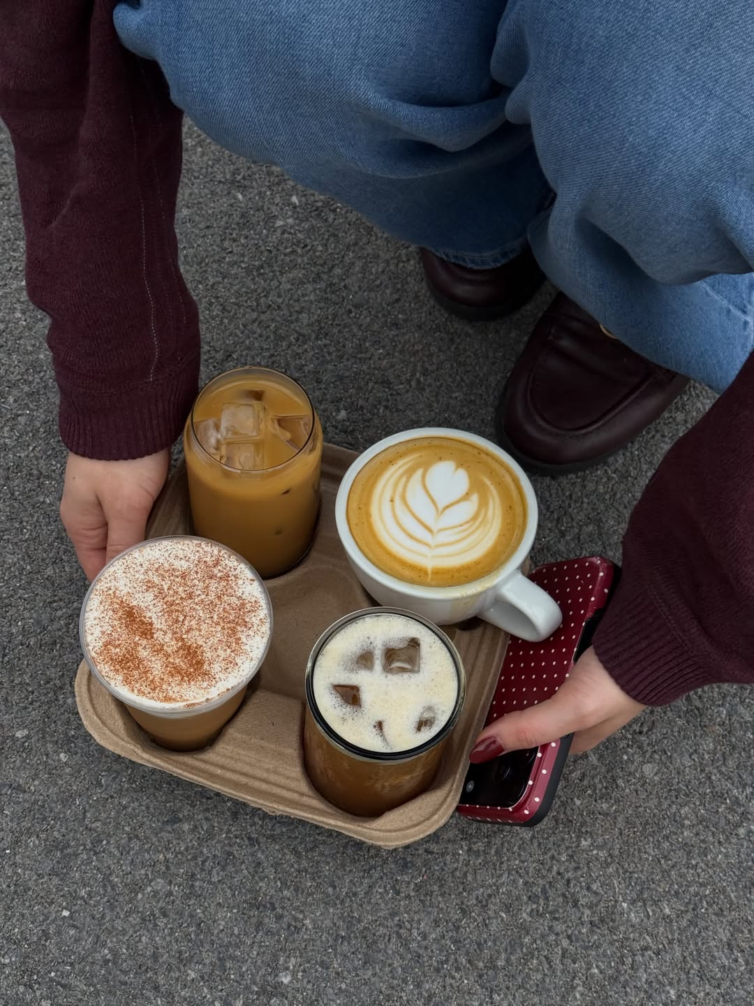 Four hot and iced coffees from Character Coffee on a drink tray, including a latte with leaf-shaped foam art.